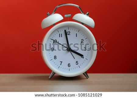 Classical style white alarm clock on wood table, red background