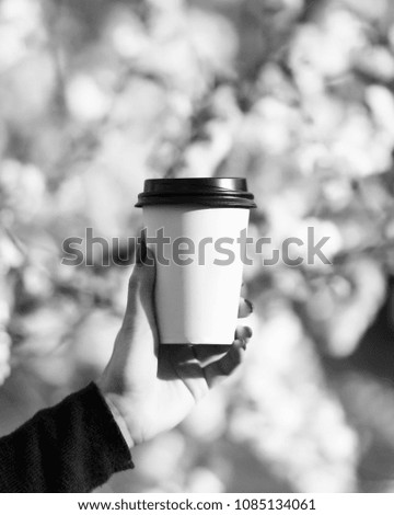 Pepper cup with coffee or tea with space for text in a woman's hand. Black and white photo. Conceptual picture