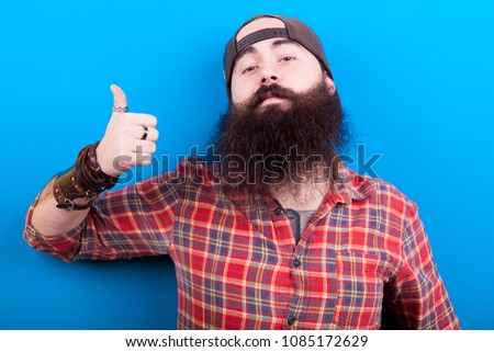 Man with long beard showing thumbs up to the camera on blue background