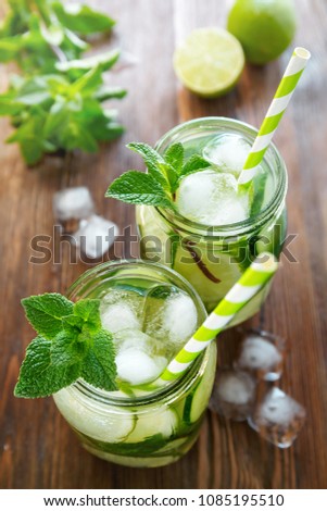 Two jars of fruit and herb infused water with cucumber, lime, mint and ice pieces on a wooden table. The concept of detox and weight loss.