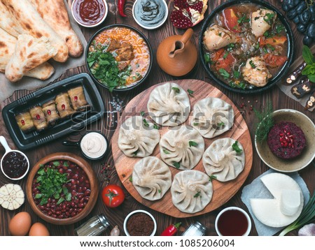 View from above of georgian cuisine on brown wooden table. Traditional georgian cuisine and food - khinkali, kharcho, chahokhbili, phali, lobio and local sauces - tkemali, satsebeli, adzhika. Top view Royalty-Free Stock Photo #1085206004