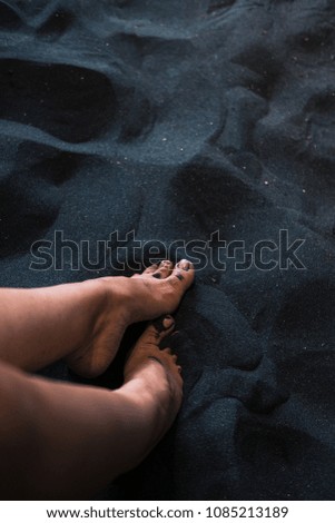 Woman's feet on black sand from above.