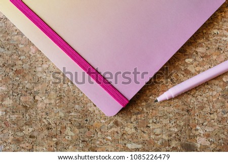 Pink school notebook with elastic band and a pen on a background made out of cork