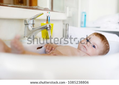 Cute adorable baby taking bath in washing sink and grab water tap.