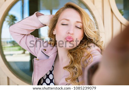 Portrait of beautiful retro woman taking selfies photos, smiling fun networking outdoors, throwing kiss. Vintage female tourist using technology, hand holding camera lens, recreation leisure lifestyle