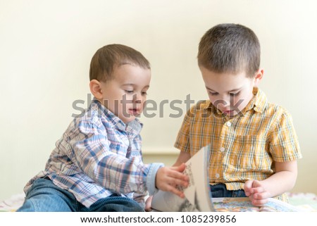 Two cute little boys are studying a book. Two little boys in shirts with a book. concept of education