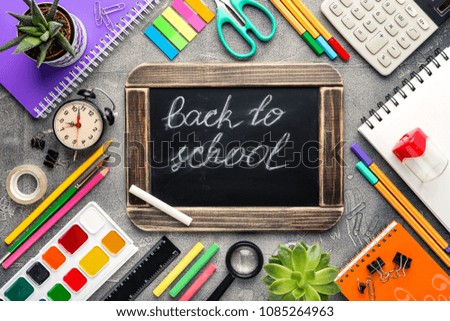 School supplies and black chalk board on a gray concrete table, a place for your text, top view