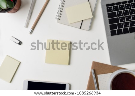 Top view of office workplace. White desk with copy space. Flat lay view on table with laptop, phone, notebooks, cup of coffee, flower and stickers, memopads. Creative designer concept.
