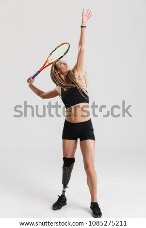 Photo of a young disabled sportswoman tennis player standing isolated over grey background play tennis.