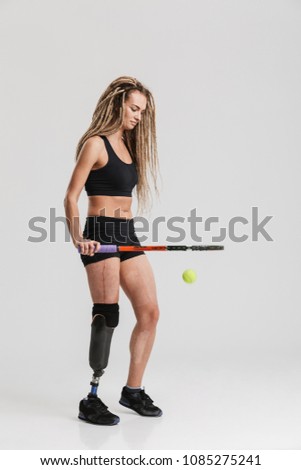 Photo of an amazing healthy young disabled sportswoman tennis player standing isolated over grey background play tennis.
