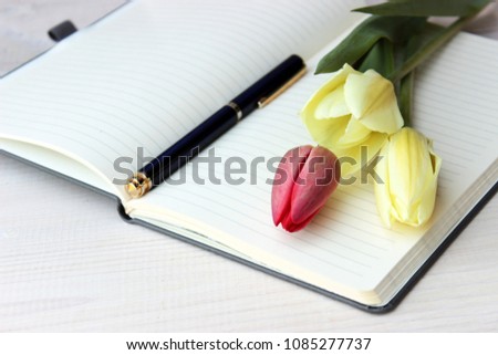 Fine romantic composition with open paper notebook with lines on pages and beautiful bouquet of spring tulips. Dreaming concept. Day planing theme. Simple composition on white wooden background