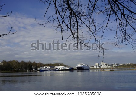 Silhouette of leafless tree branches with background of big cruise ships parking in the river and white fluffy clouds on blue sky on a sunny day.