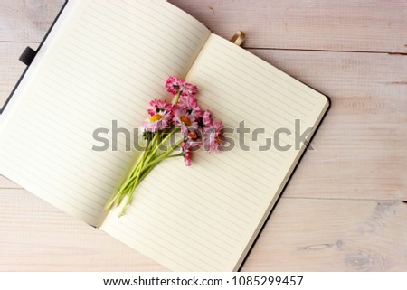 Fine romantic composition with open paper notebook with lines on pages and beautiful bunch of pink daisy. Dreaming concept. Day planing theme. Simple composition on white wooden background