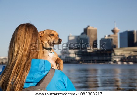 Girl holding her little dog, Chihuahua, and enjoying the beautiful view of the downtown city. Taken in Stanley Park, Vancouver, British Columbia, Canada.