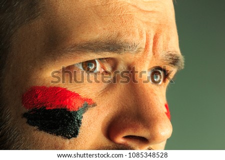 Portrait of a man with the flag of the Germany painted on him face. Young male caucasian model closeup. Football, soccer, fan concept. Human emotions, facial expressions concepts