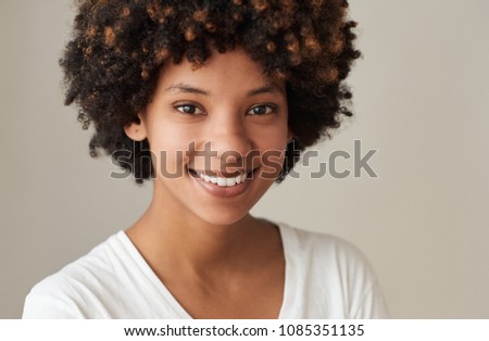 Closeup portrait of a smiling young African woman with an afro and natural complexion standing against a gray background
