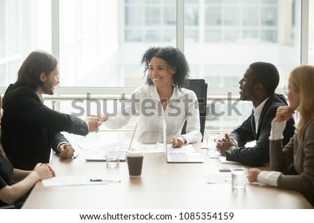 Friendly smiling african businesswoman handshaking caucasian businessman at diverse group meeting, mixed race black female boss welcoming new partner or executive team member shaking hands 
 boardroom Royalty-Free Stock Photo #1085354159