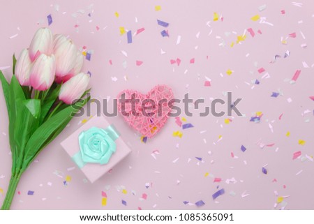 Flat lay aerial image of items mothers day holiday background concept.Table top view gift box & tulip flower with heart shape on modern rustic pink paper backdrop with copy space.Pastel tone design.