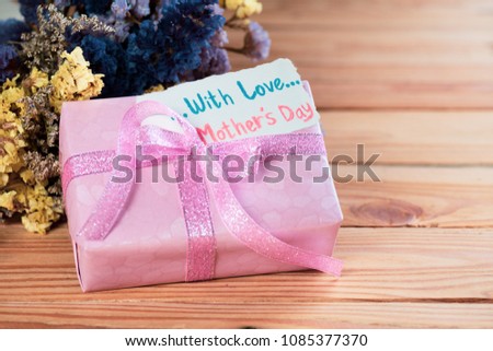 Happy mother's day concept. Gift box with flower, paper tag with Love Mother's Day text on wooden table background.