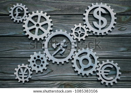 office worker inside a gear wheel surrounded by gears with signs of currencies on a wooden background. business. finance. businessman, teamwork, cooperation, strategy, industry, innovation.