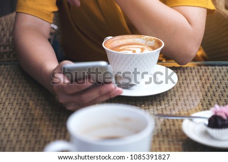 Closeup image of a woman using and looking at smart phone with coffee cups in cafe
