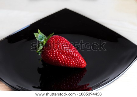 one strawberry on a black plate on a white background