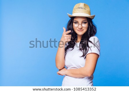 Beautiful Brunette in white t-shirt and glasses on blue background shows finger gesture to camera
