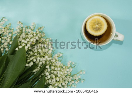 Top view of the cup of tea with the slice of lemon and lily of the valley flowers on the pastel light background. Copy space.