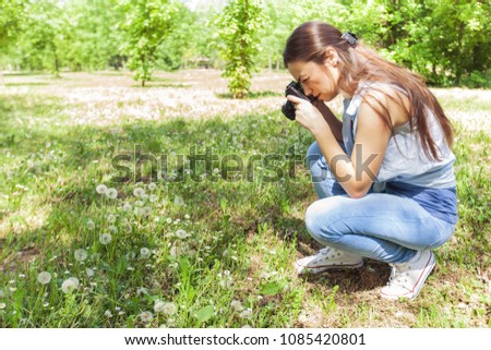 Young woman making picture of dandelion with vintage camera, female amateur photographer taking photo in nature