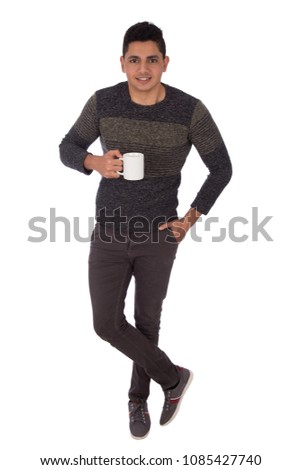 Full-length shot of a young man standing crossed legs and holding a mug smiling, isolated on a white background.