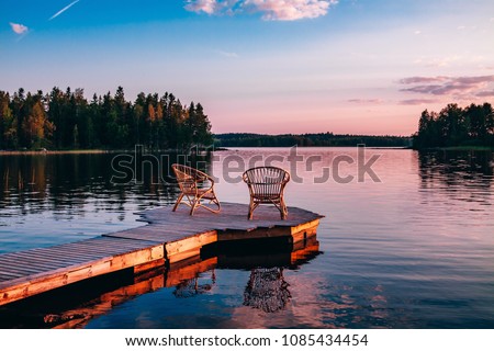 Two wooden chairs on a wood pier overlooking a lake at sunset in Finland Royalty-Free Stock Photo #1085434454
