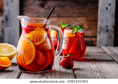 Homemade red wine sangria with orange, apple, strawberry and ice in pitcher  and glass on rustic wooden background Royalty-Free Stock Photo #1085435402