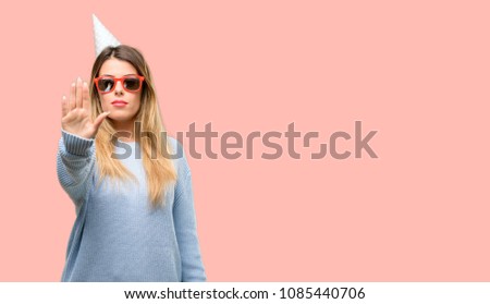 Young woman celebrates birthday annoyed with bad attitude making stop sign with hand, saying no, expressing security, defense or restriction, maybe pushing