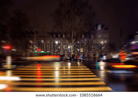 Blurry motion image of people waiting to cross at lights in Republique square at night in Paris.