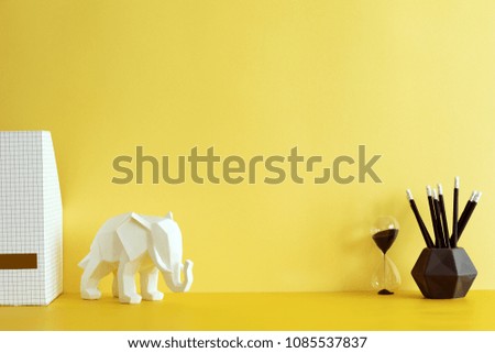 Yellow interior with elephant figure, hourglass and office accessories. Creative space with yellow background wall.
