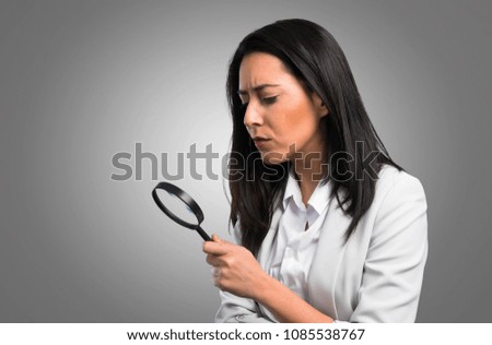 Pretty woman with magnifying glass on grey background