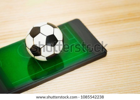 A toy soccer ball on a smartphone with a picture of a green field. Concept of the game of football