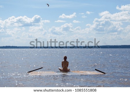 A girl in the summer meditates on a platform covered with water, installed in water near the shore with background of clouds. photo with copyspace