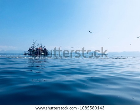 Fishing boat and fishing net over blue sea and clear sky with birds flying overhead. Royalty-Free Stock Photo #1085580143