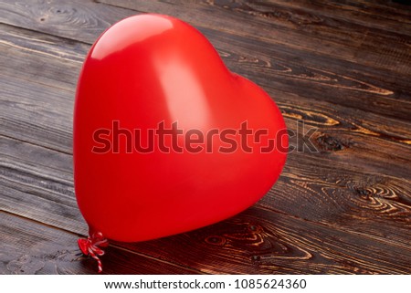 Heart shaped balloon on wooden background. Red balloon in a shape of heart filled with oxygen on brown wooden background.