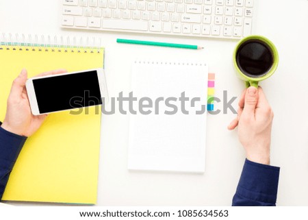 white desk, male hands, guy uses white smart phone, man holding Cup of coffee, office supplies,  white background with copy space, for advertisement, top view