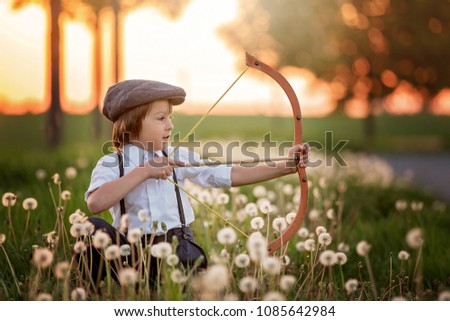 Portrait of child playing with bow and arrows, archery shoots a bow at the target on sunset Royalty-Free Stock Photo #1085642984