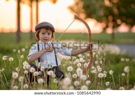 Portrait of child playing with bow and arrows, archery shoots a bow at the target on sunset Royalty-Free Stock Photo #1085642990