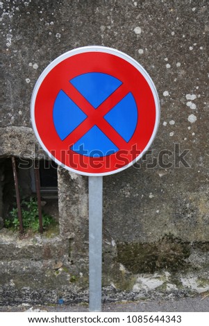 Close up outdoor view of a traffic sign indicating: no parking. Blue and red circular symbol placed in a french street, in front of a dark grey wall. Abstract graphic image with vivid colors.