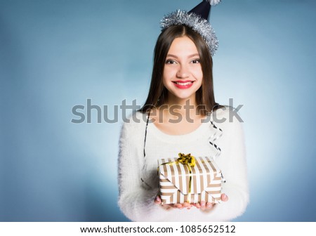 happy young girl with a cap on her head holds a New Year gift and smiles