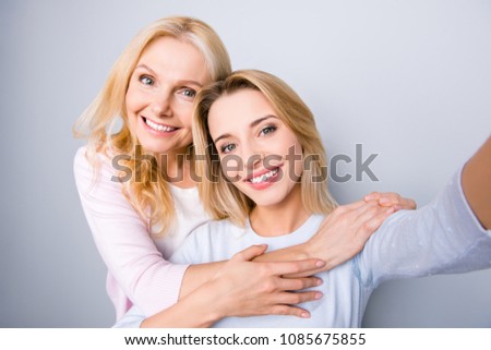 Self portrait of stylish trendy cute lovely grandma and daughter, warm hugs, shooting selfie on front camera, family with one single parent, isolated on grey background