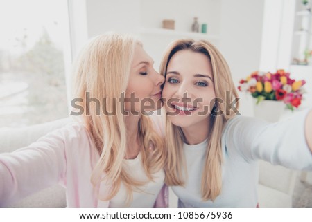 Self portrait of cheerful lovely cute charming mother kissing in cheek daughter family with one parent shooting selfie on front camera enjoying time meeting holiday day indoor