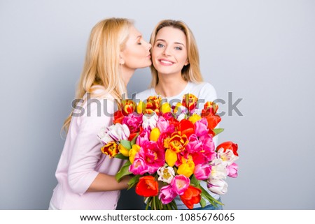 Birthday girl enjoying kiss in cheek congrats from her lovely charming mother holding big colorful bouquet of tulips comfort idyllic pleasure happiness concept isolated on grey background