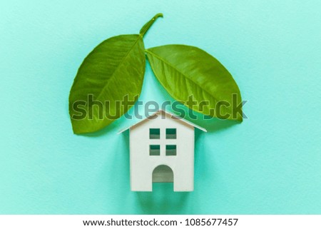 Miniature toy model house with green leaves on blue pastel colourful trendy backgdrop. Eco Village, abstract environmental background. Real estate mortgage property insurance dream home ecology