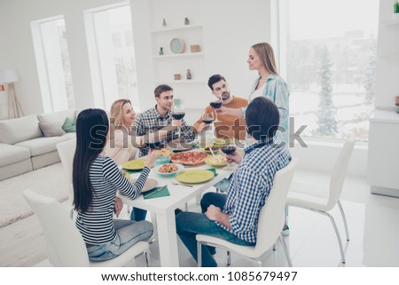 Be happy and healthy my best friend! Beautiful girl standing saying toast to her sister, visitors, guests raise glasses with red wine listening wishes ready to clink, indoor, in apartment